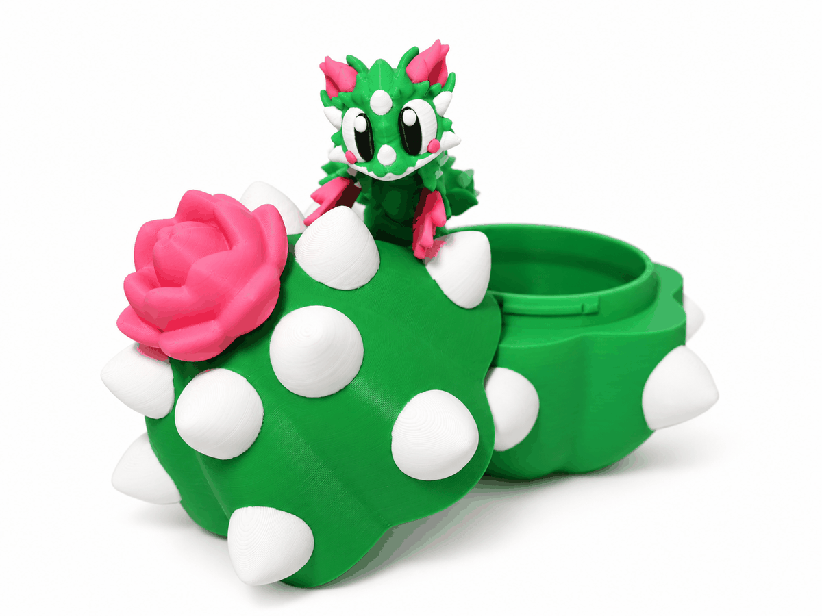 Drachenfigur ProtoDrache – Rosenkaktus mit grünem Körper, weissen Stacheln, pinker Rose und beweglichem Kopf.
