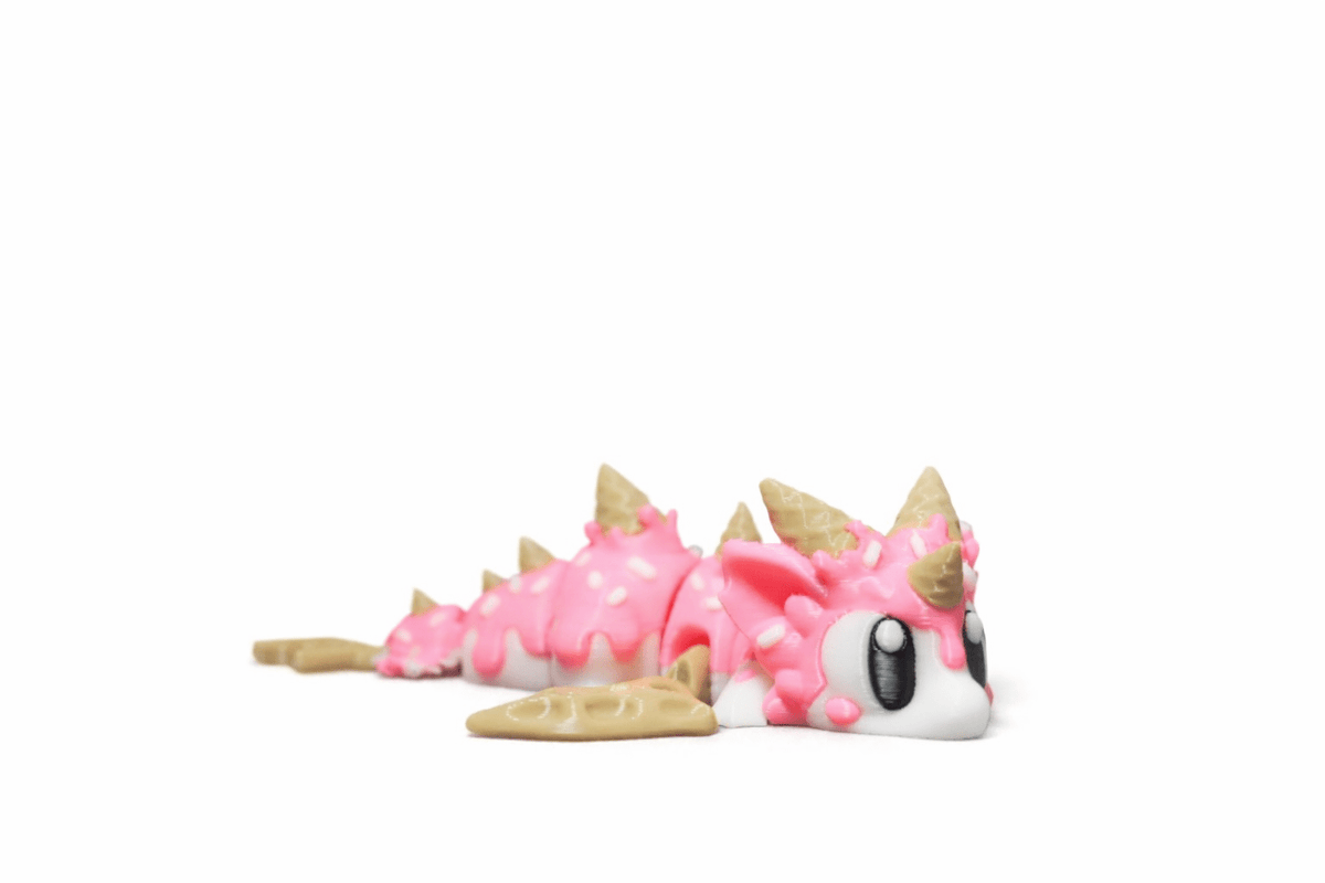 IceCream Drache als rosa-weiße Kunststofffigur mit Streuselmuster, goldfarbenen Hörnern und großen Augen