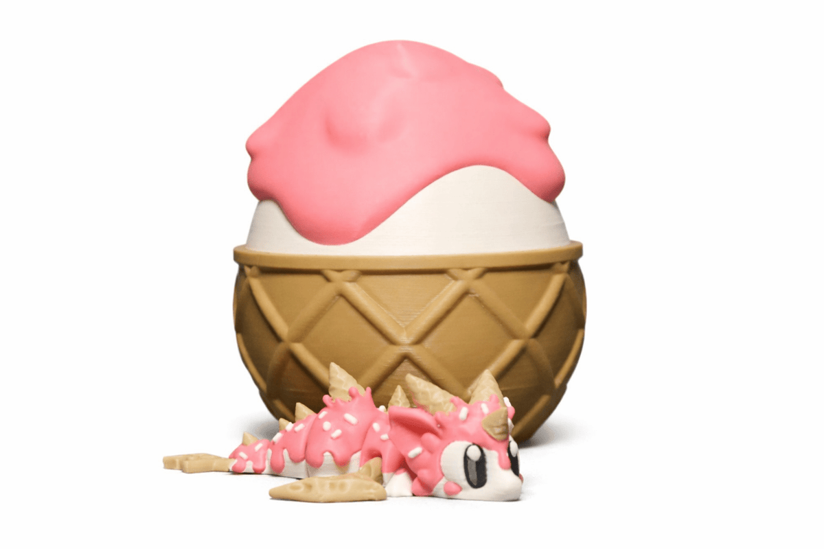 IceCream Drache als rosa-weiße 3D-Druckfigur mit Hörnern und Streuseln, dazu ein brauner Waffelbecher mit Eis