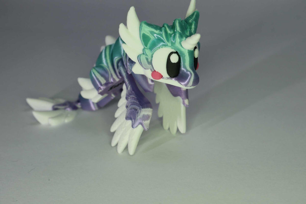Drachenfigur ProtoDrache Auroria aus 3D-Druck in Türkis und Violett mit weißen Hörnern, großen Augen und gegliedertem Schwanz